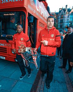 two men in red jackets standing next to a bus