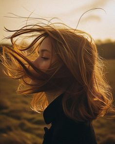 a woman with her hair blowing in the wind on an open grassy field at sunset