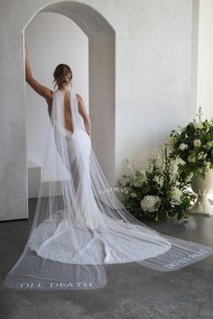 a woman in a white wedding dress with a veil on her head and flowers behind her back