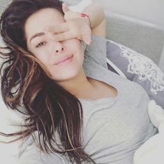 a woman laying on top of a bed holding her hand up to her forehead and looking at the camera