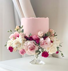 a pink cake with white and red flowers on the top is sitting on a table