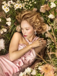 a woman in a pink dress laying on the ground surrounded by flowers