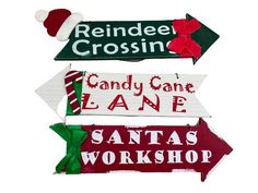 three wooden signs with santa's workshop written on one sign and candy cane lane painted on the other