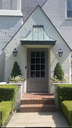 the front entrance to a white house with trimmed hedges