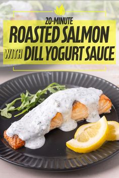 salmon with dill yogurt sauce on a black plate next to lemon wedges