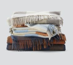 several blankets stacked on top of each other in different colors and patterns, with fringes