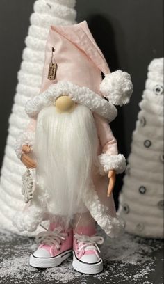 a white and pink gnome doll standing in front of two white trees with snow on them