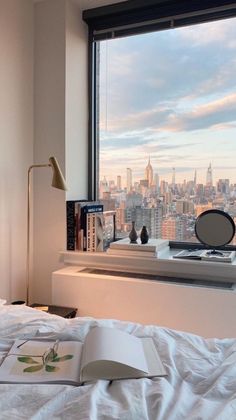 an open book sitting on top of a bed in front of a window overlooking the city