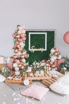 a table topped with cake and balloons next to a green wall covered in greenery