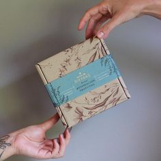 two hands reaching out to open a brown and blue box with floral designs on it