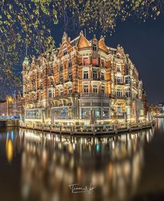 an old building is lit up at night by the water with lights reflecting off it's windows