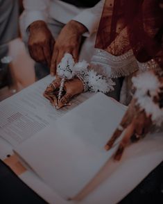 two people sitting at a table with papers and flowers in their hands, one person is writing on the paper