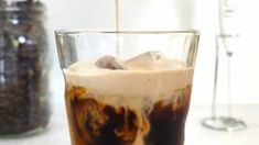 an iced drink being poured into a glass with ice and coffee beans in the background