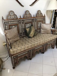 an ornate wooden bench with pillows on it in front of a wall clock and mirror