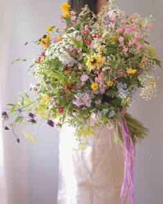 a woman holding a bouquet of wildflowers and other flowers in her hands,