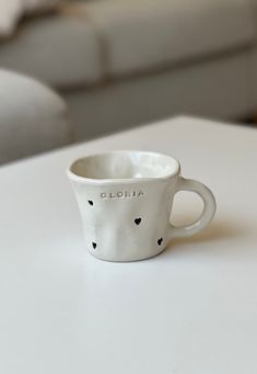 a white coffee cup sitting on top of a table next to a couch with the word cloudia written on it