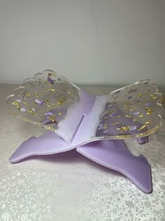 a purple and gold butterfly shaped object sitting on top of a white tablecloth covered table