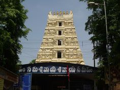 a tall tower with statues on it in the middle of a street near some trees