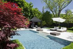 an outdoor pool with lounge chairs and umbrellas next to it, surrounded by trees