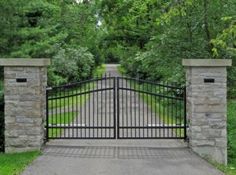 an iron gate with stone pillars leads into a driveway