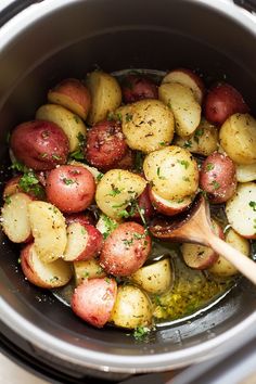 the potatoes are being cooked in the crock pot with a wooden spoon on the side