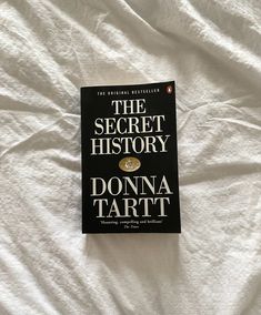 a book sitting on top of a bed covered in white sheets with the title, the secret history