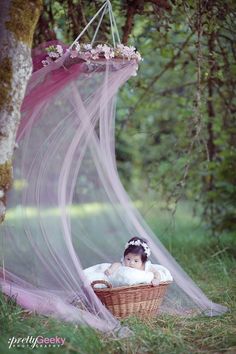 a baby sitting in a basket on the ground with a pink net hanging from it's side