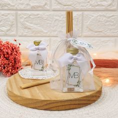 two small bottles with white bows on them sitting on a wooden tray next to some flowers