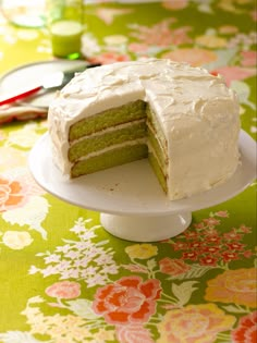 a green cake with white frosting sitting on top of a flowered table cloth