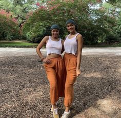 two young women standing next to each other in front of trees and dirt ground with their arms around each other