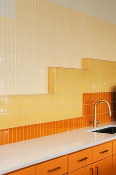 a kitchen with yellow and orange tiles on the wall, sink and countertop area