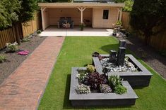 a backyard with grass, flowers and plants in the center is a brick walkway that leads to a covered patio area