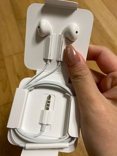 a hand holding an apple earbuds in front of a white box on a wooden floor