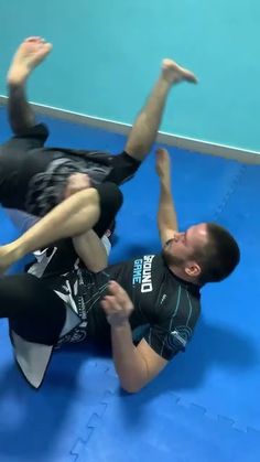 two men in black shirts are wrestling on blue mats with one man holding the other