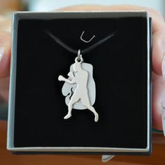 a person is holding up a silver pendant in a black box with a white dog on it