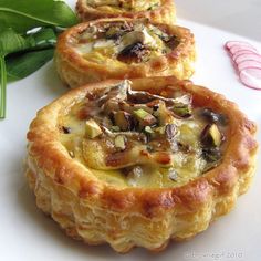 three small pastries sitting on top of a white plate next to some green leaves