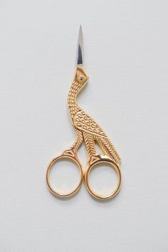 a pair of gold scissors with a bird on it's handle, sitting on a white surface