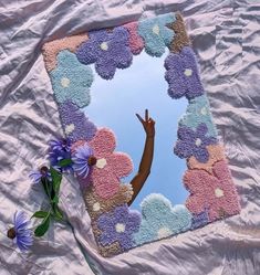 a person reaching up into the sky through a mirror with flowers in front of it