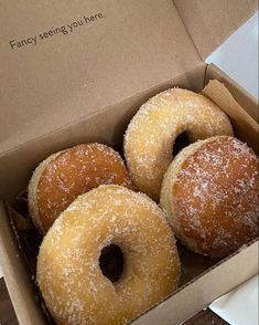 four donuts in a box with sugar sprinkled on them