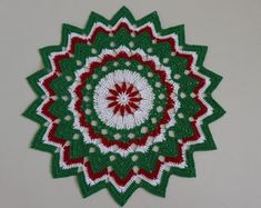 a green and red crocheted doily on a white wall with a circular design in the center