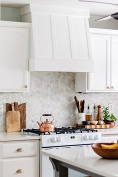 a kitchen with white cabinets and marble counter tops, including a range hood over the stove