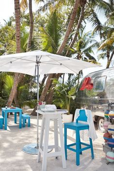 an umbrella and stools on the beach near palm trees with a van in the background