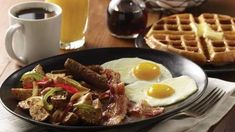 two breakfast plates with eggs, sausage and waffles on a table next to a cup of coffee