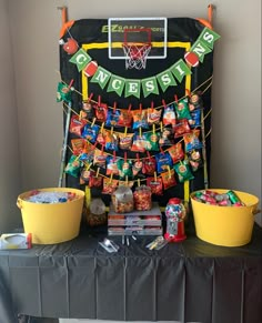 a table topped with buckets filled with candy next to a basketball net and banner