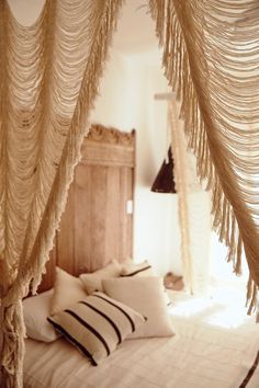 a bed with some pillows on top of it and curtains hanging over the headboard