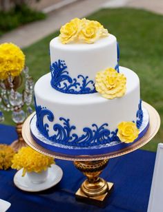 a blue and white wedding cake with yellow flowers on the top is sitting on a table