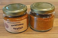 two jars filled with ground spices sitting on top of a wooden table next to each other