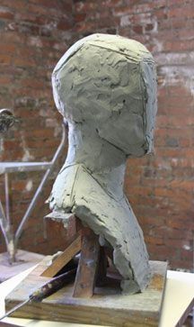 a clay sculpture sitting on top of a piece of wood next to a brick wall