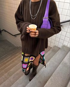 a woman in brown sweater and colorful skirt holding a cup