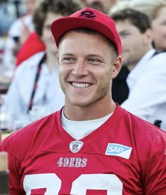 a man in a red football uniform is smiling for the camera while people are sitting behind him